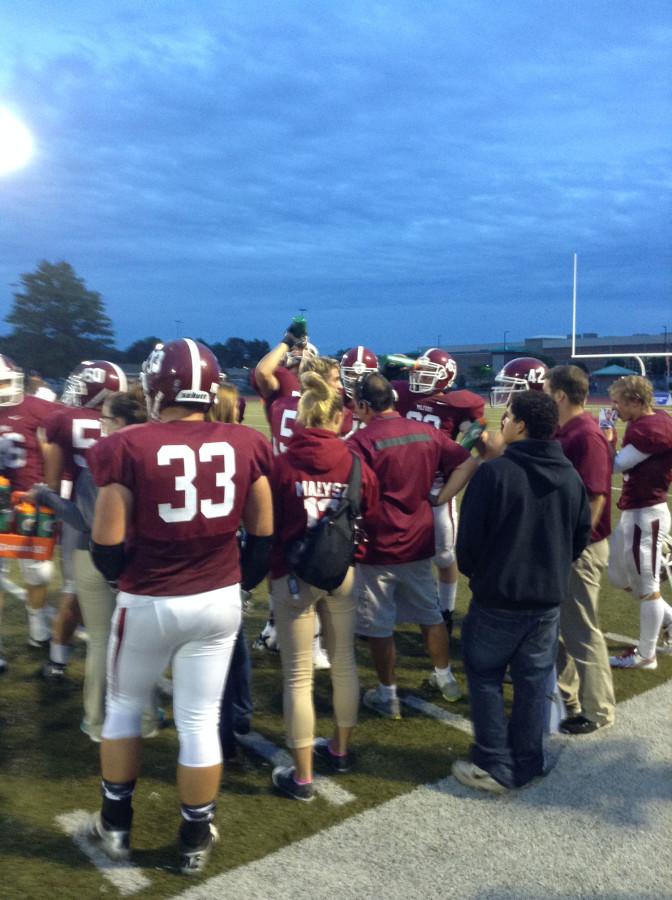 Milford Football players and staff gather on the sideline during a time out to discuss strategy and quench their thirsts during the game.