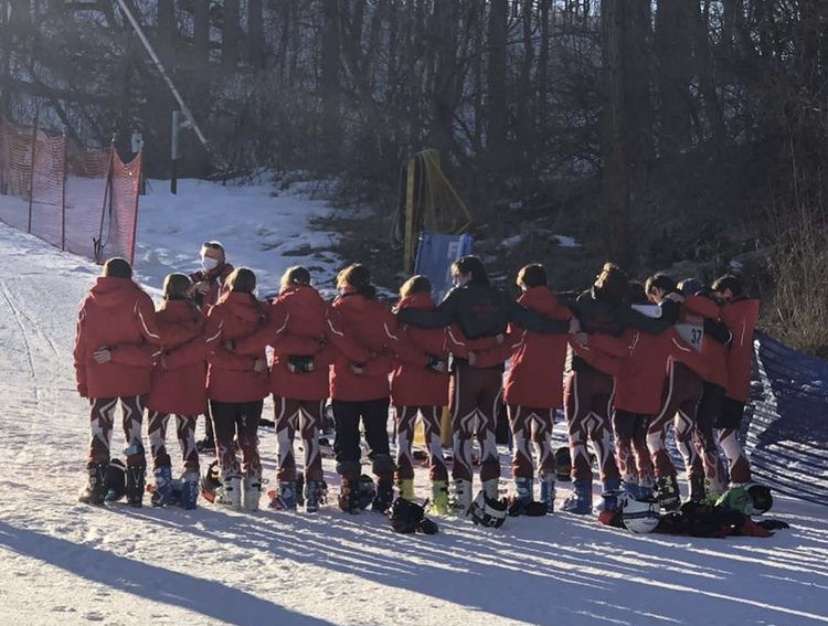 Boys and girls ski teams arm-in-arm before a run.