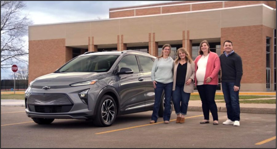 Lori Gleason with former students Autumn Lagowski, Ashley Legato and Ryan Legato posing by the Chevy car in front of Milford high school.